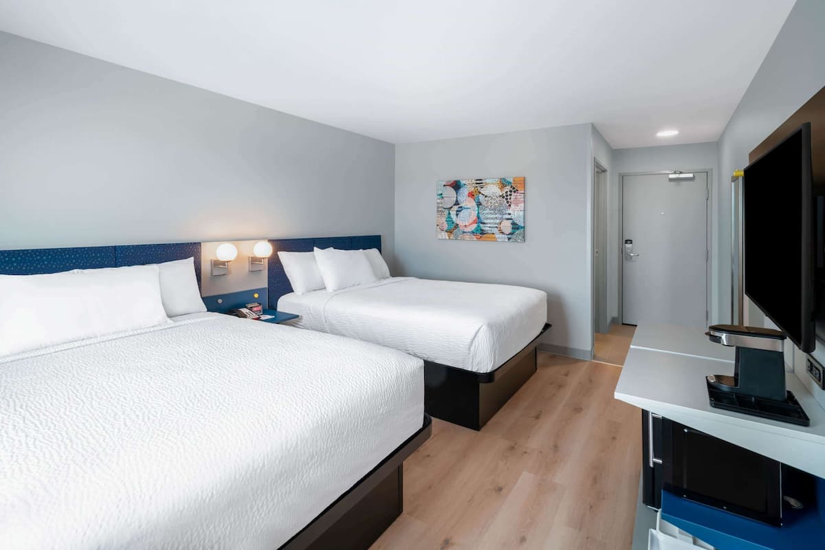 A hotel room with two beds, a flat-screen TV, a painting on the wall, and a door leading to the bathroom.