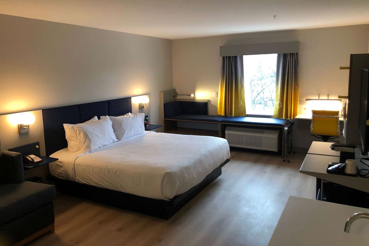 A hotel room with a large bed, bedside tables, a desk, a chair, a TV, and a window with curtains.