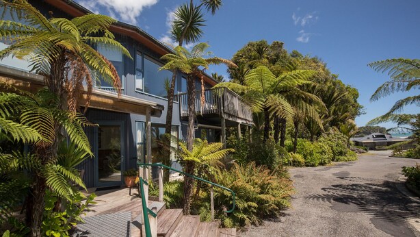 Ein modernes Haus mit einer Holterrasse, umgeben von üppiger Vegetation, darunter Farne und Palmen.