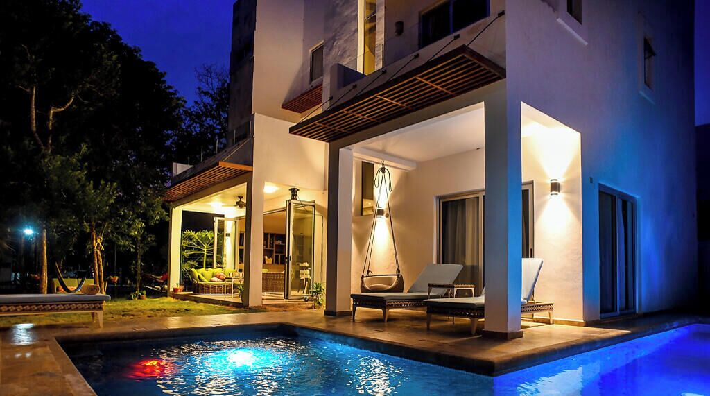 Un espace moderne aménagé au bord de la piscine, offrant une vue dégagée sur celle-ci, avec des chaises longues et un intérieur bien éclairé.