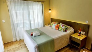 A neatly made bed with a green blanket, a floral pillow set, and a bottle of wine on a bedside table.