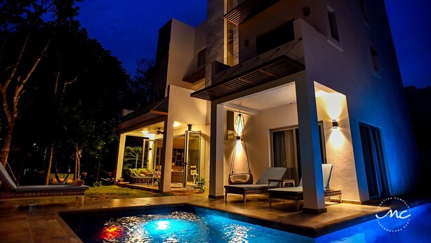 A modern two-story building with a swimming pool, outdoor seating, and a well-lit entrance.