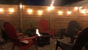 Eine Terrasse im Freien mit Feuerschale, Lichterketten und Adirondack-Stühlen.