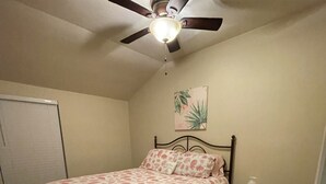 Ein Schlafzimmer mit Bett, Nachttisch, Deckenventilator und Wandpflanze.