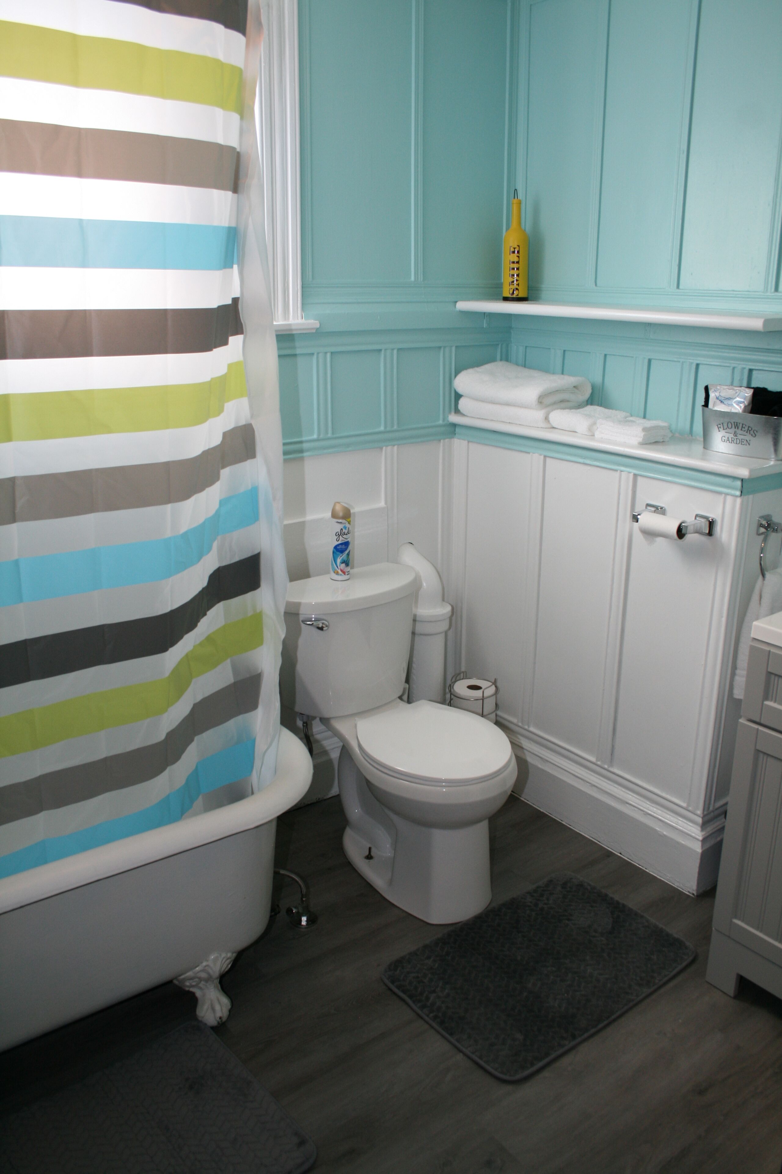 Une salle de bain avec un rideau de douche à rayures, des toilettes, un bidet et une étagère contenant des articles de toilette.