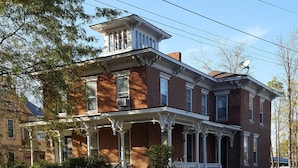 A large, two-story brick house with a prominent porch and a small tower-like structure on the roof. - The Keuka at Red Brick Manor (Seneca Falls)