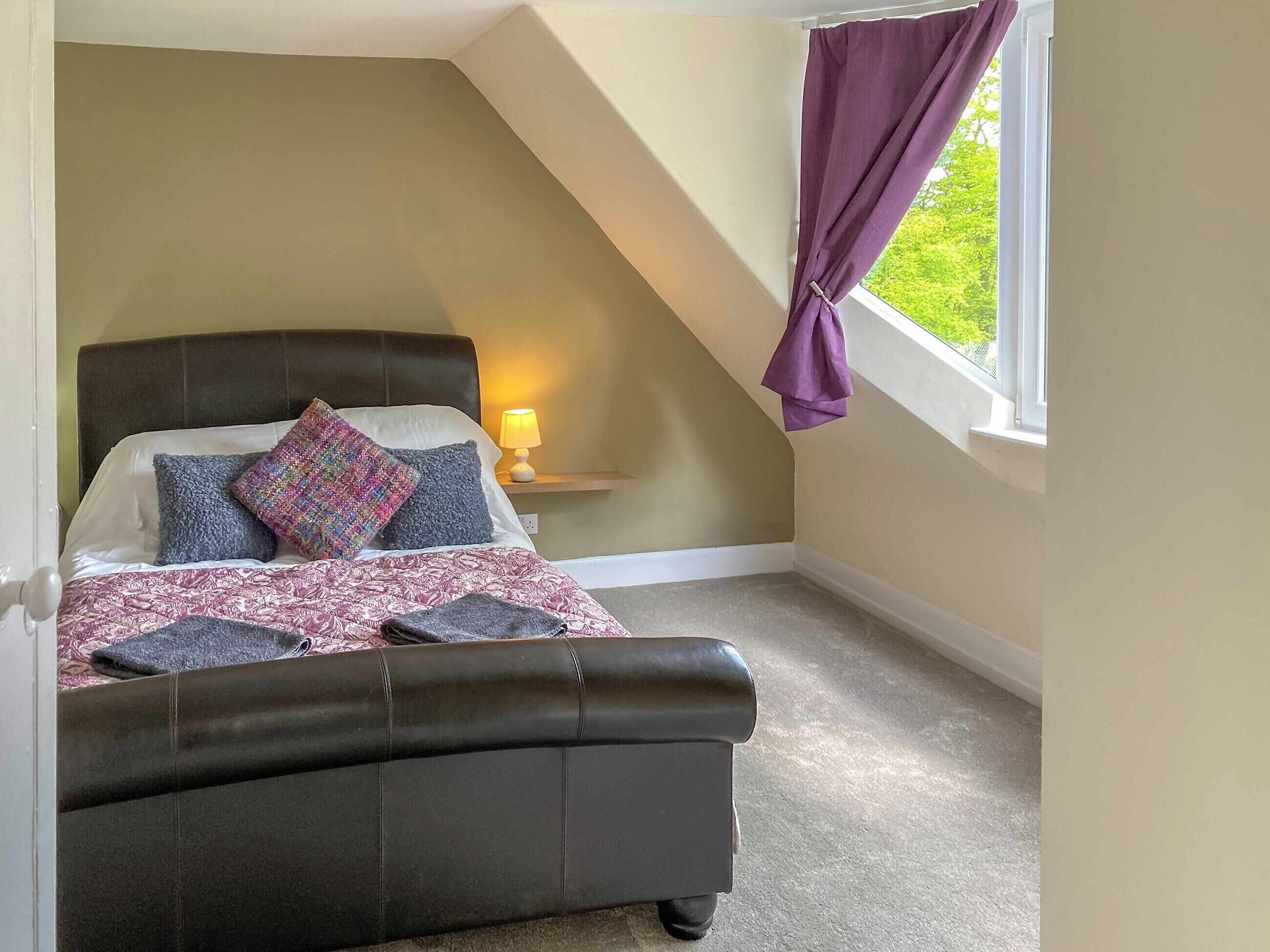 Une chambre à coucher avec un lit, une table de chevet, une lampe et une fenêtre avec des rideaux.