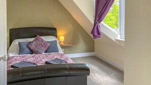 Quarto com cama, mesa de cabeceira, abajur e janela com cortinas.