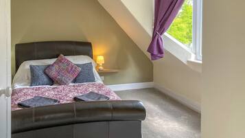 Une chambre à coucher avec un lit, une table de chevet, une lampe et une fenêtre avec des rideaux.