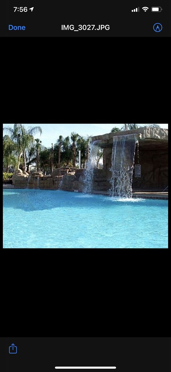 A pool with a waterfall feature surrounded by palm trees.
