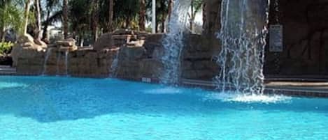 A swimming pool with a waterfall feature, surrounded by palm trees.