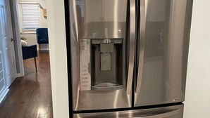 Un refrigerador de acero inoxidable con dispensador de agua, ubicado en un pasillo con piso de madera y una puerta que da a otra habitación.