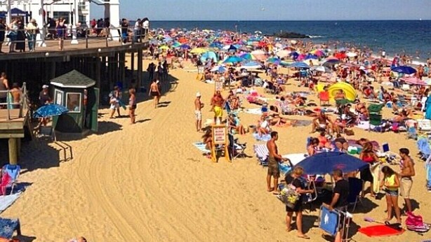 Una playa concurrida con una torre de salvavidas y un muelle.