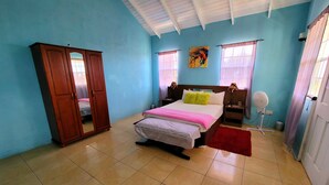 Un dormitorio con cama, armario, espejo, ventilador y un cuadro en la pared.