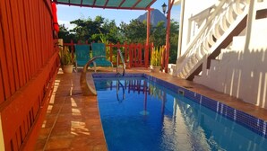 Una piscina con borde de azulejos, rodeada por una valla roja y plantas en macetas.