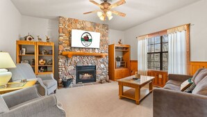 A cozy living room with a stone fireplace, wooden furniture, and a ceiling fan. - Walk-In 2BR Grand Mountain Cabin with Ozark Views | Sleeps 6 (Branson)