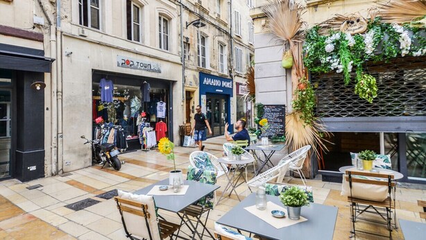 An outdoor café area with tables and chairs, a motorcycle parked outside a clothing store, and a person walking by.