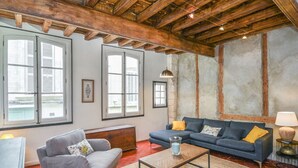 A living room with a sofa, a coffee table, and a lamp. There are windows with shutters and a picture frame on the wall.