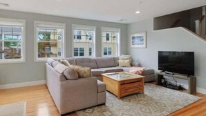 A modern living room with a sectional sofa, a coffee table, and a flat-screen TV. - Make your summer memories here! (Wells)