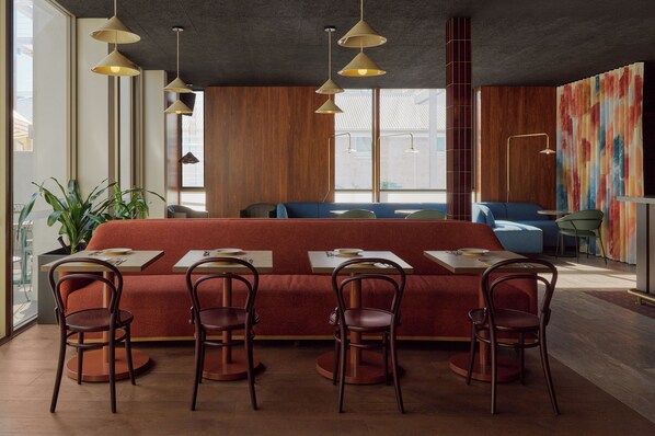 Un restaurante moderno con una larga mesa común, cabinas individuales e iluminación colgante.