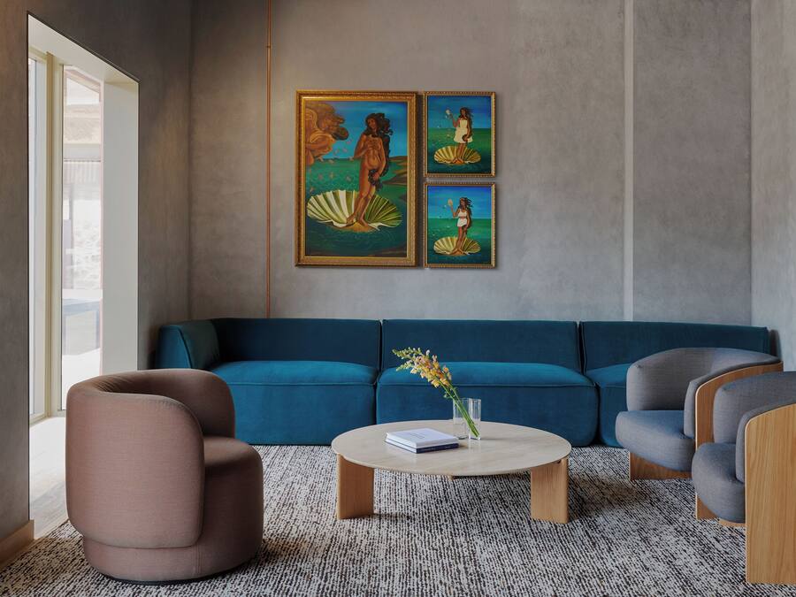 A modern living room with a blue sofa, a round coffee table, and a pink armchair. There are two framed paintings on the wall.