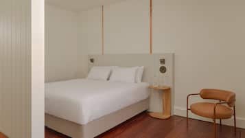 A bedroom with a bed, a wooden nightstand, a chair, and a wall-mounted light fixture.