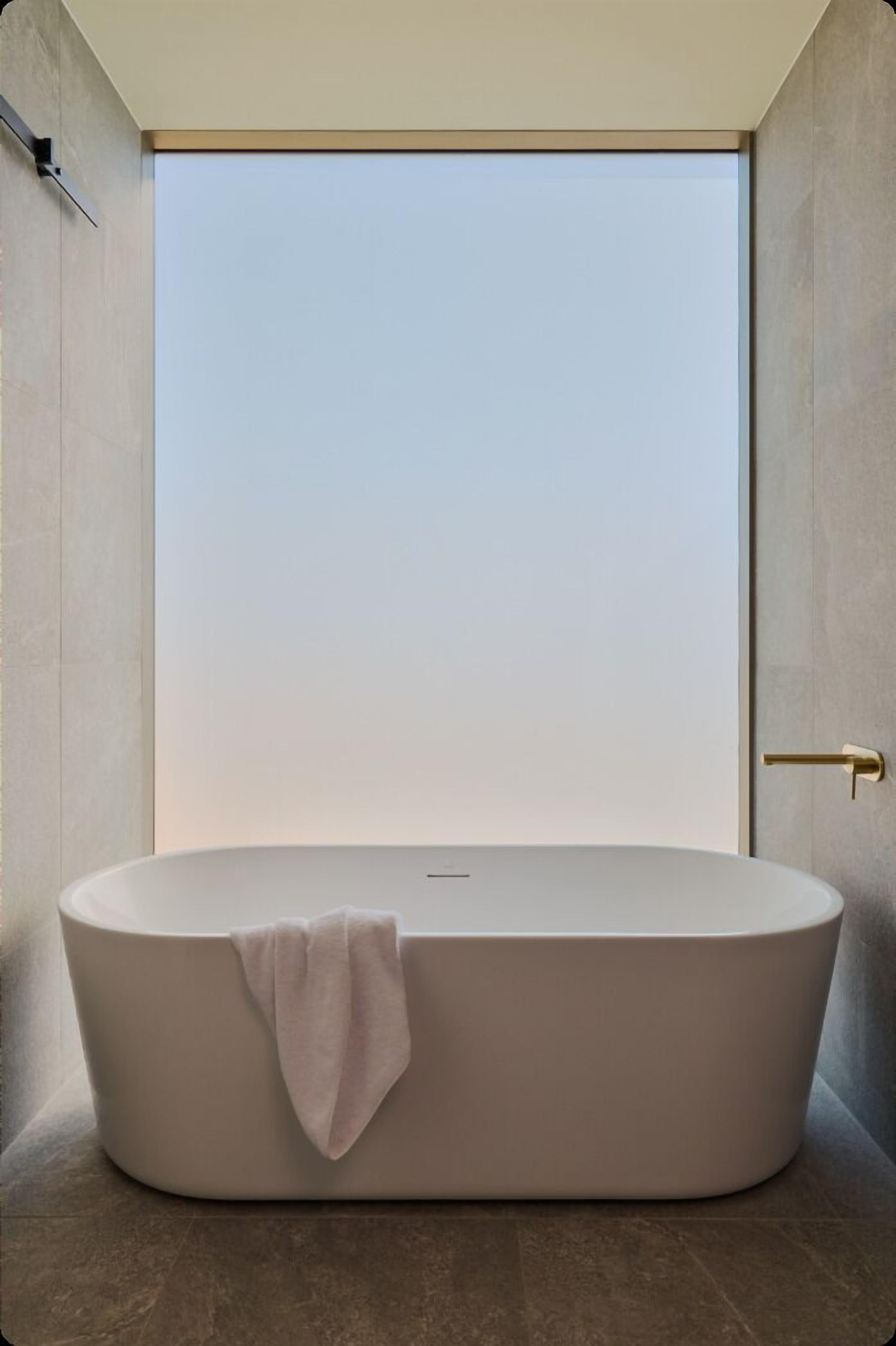 A modern bathroom with a freestanding bathtub, a towel, and a view of the sky.