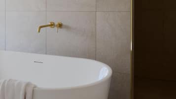 A modern bathroom with a freestanding bathtub, a gold faucet, and beige tiles.