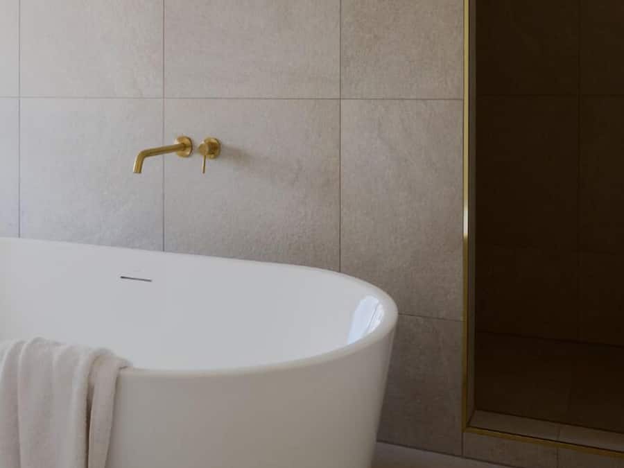 Un baño moderno con una bañera independiente, un grifo dorado y baldosas color beige.