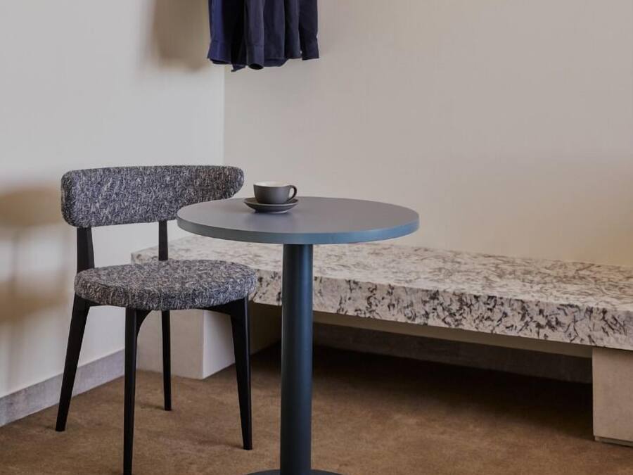 A small room with a round table, a chair, a bench, and a coat rack with two jackets.