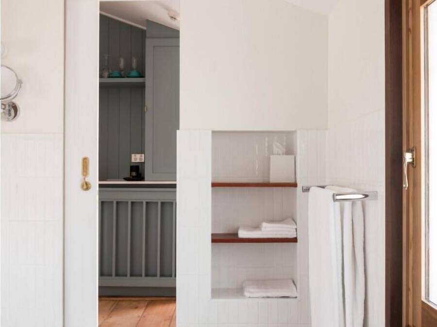 A modern bathroom with white tiles, a marble floor, a wooden door, and a view into a kitchen area.