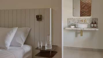A bedroom with a bed, bedside table, and a bathroom with a sink and mirror.