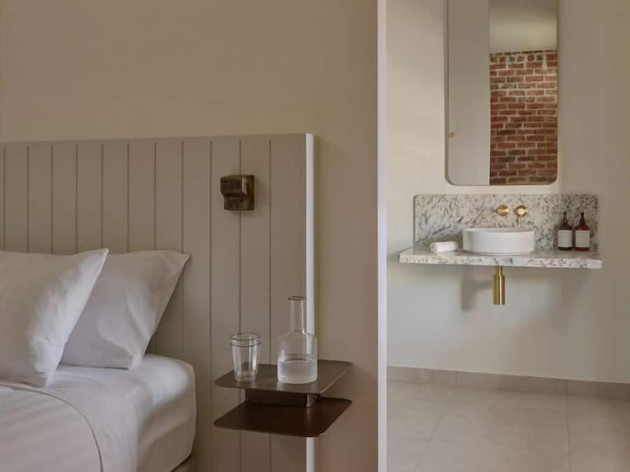 Un dormitorio con cama, mesita de noche y baño con lavamanos y espejo.