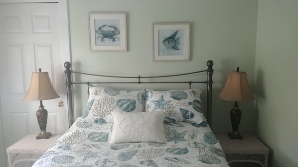 Una cama con una colcha estampada, dos cuadros en la pared y dos lámparas de noche.