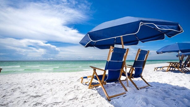 Una playa con sombrillas azules y sillas de madera.