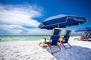 A beach with blue umbrellas and wooden beach chairs.