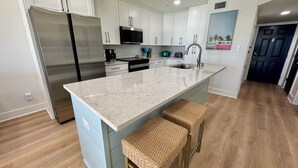 Una cocina moderna con armarios blancos, electrodomésticos de acero inoxidable, encimera de mármol e isla integrada con taburetes de bar.