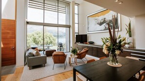 A modern living room with a large window, a dining area, and a kitchen. - Lake Edge | Central lakefront apartment | 3 bed (Wanaka)