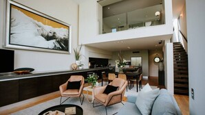 A spacious living area with a high ceiling, a dining area, and a staircase leading to an upper level. - Lake Edge | Central lakefront apartment | 3 bed (Wanaka)