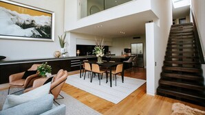 A modern living room with a dining area, a staircase, and a kitchen in the background. - Lake Edge | Central lakefront apartment | 3 bed (Wanaka)
