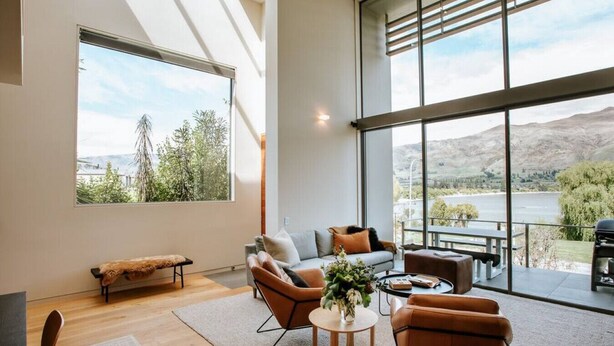 A spacious living room with a large window offering a view of a lake and mountains. - Lake Edge | Central lakefront apartment | 3 bed (Wanaka)