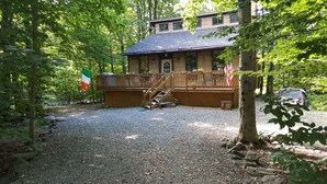 A lodge with a wooden deck, a stone staircase, and a gravel driveway surrounded by trees. - House located in the heart of the Poconos and convenient to all!!!! (Pocono Pines)