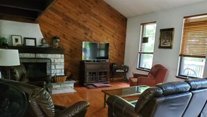A cozy living room with a fireplace, leather sofas, a television, and a dining area. - House located in the heart of the Poconos and convenient to all!!!! (Pocono Pines)