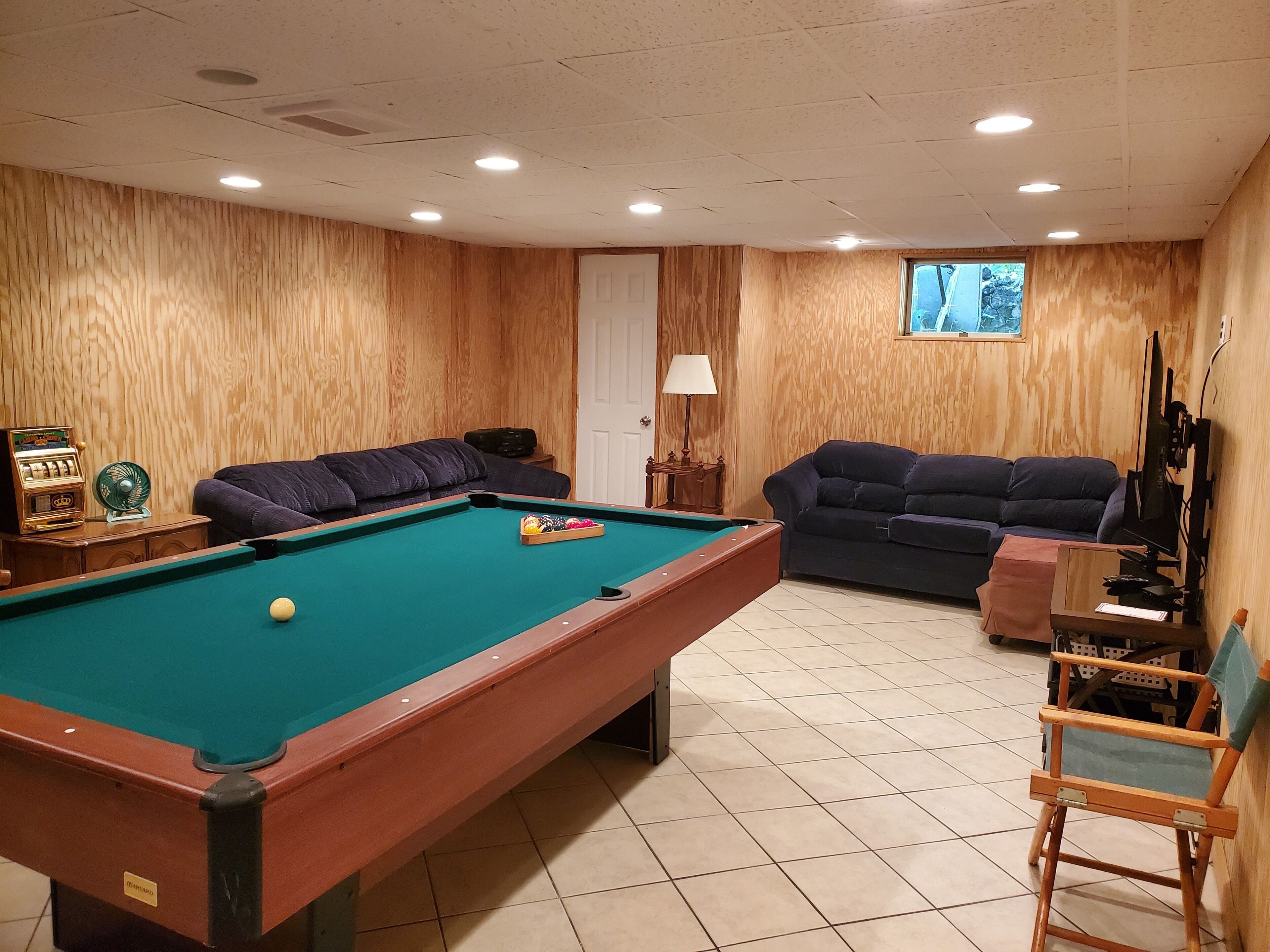 Mesa de billar en una habitación con paredes de madera y suelo de baldosas. Hay dos sofás y una silla.