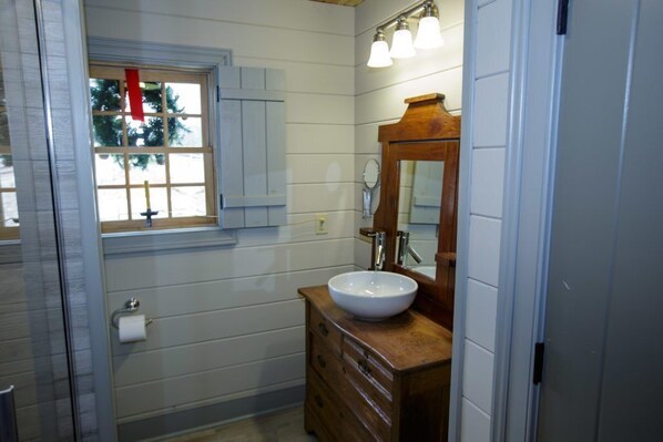 Une salle de bain avec un meuble-lavabo en bois, un lavabo blanc, un miroir et une fenêtre donnant sur des arbres.