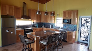 Una cocina con armarios de madera, una isla central con taburetes de bar, un refrigerador de acero inoxidable y un microondas.