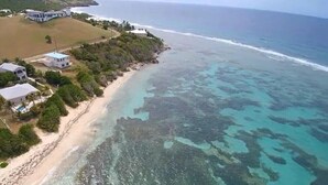 Vista aérea de una propiedad costera con playa, aguas turquesas cristalinas y varios edificios.
