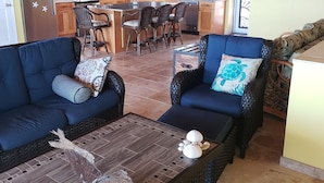 Amplia sala de estar con dos sofás azul oscuro, una mesa de centro con objetos decorativos y una cocina al fondo con gabinetes de madera y un salpicadero azulejado.