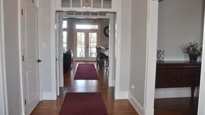 Un couloir doté d’un plancher en bois, d’un tapis rouge, d’un coin repas avec des chaises et une table, et d’une commode en bois foncé.