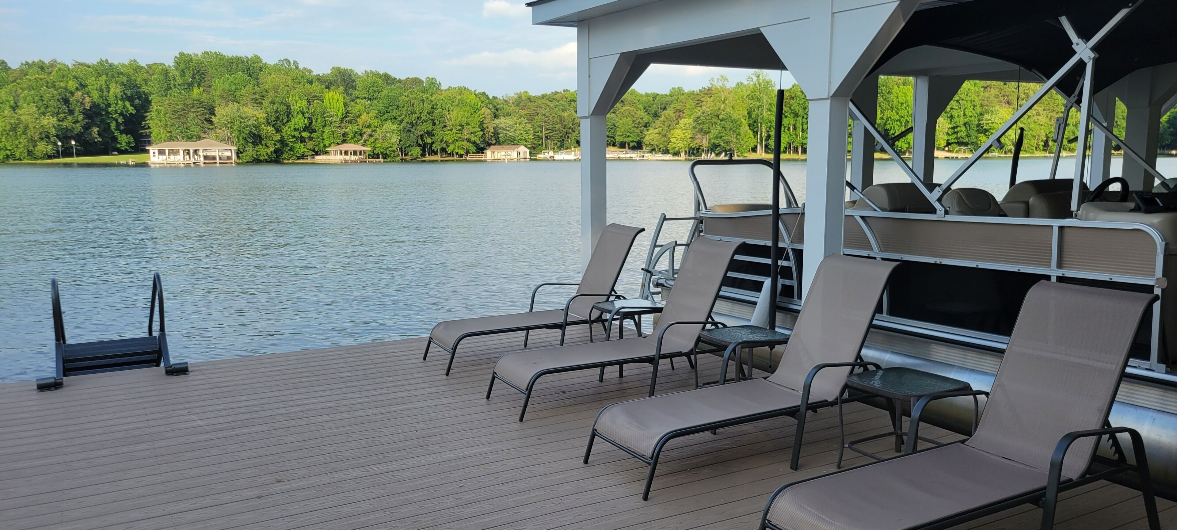 A deck with lounge chairs and a covered area overlooking a lake with buildings in the background.